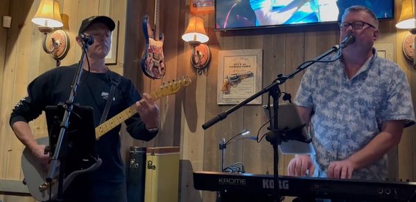 Two men performing music with guitar and keyboard in a cozy indoor setting.