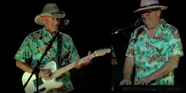 Two musicians in Hawaiian shirts playing guitar and keyboard on stage.
