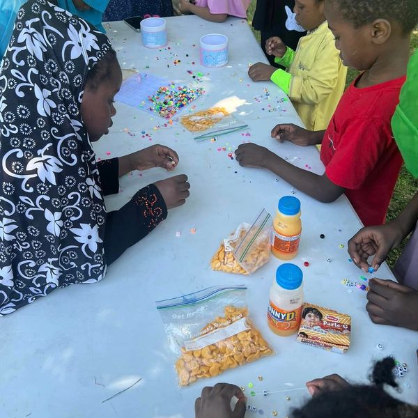 Children crafting with beads and snacks on table.