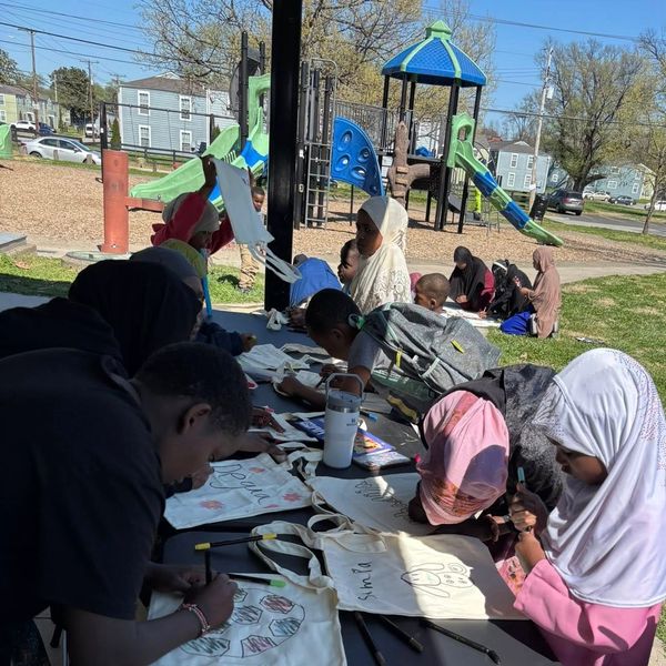 Children painting and writing on tote bags outdoors.