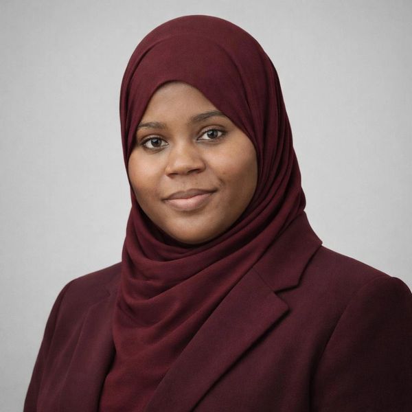 Confident woman wearing a maroon hijab and blazer against a plain background.