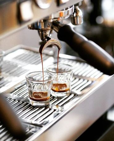 Espresso flowing into two small glasses from a machine.