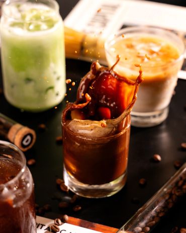 Splash of coffee in a glass with iced drinks in the background.