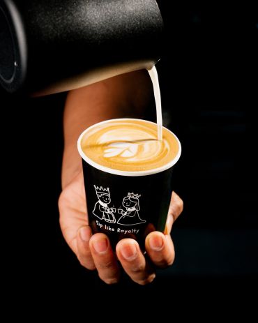 Pouring latte art in a cup with royal-themed design.