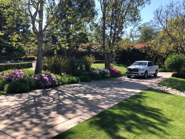 A white pickup truck parked on a driveway surrounded by lush greenery and flowers.