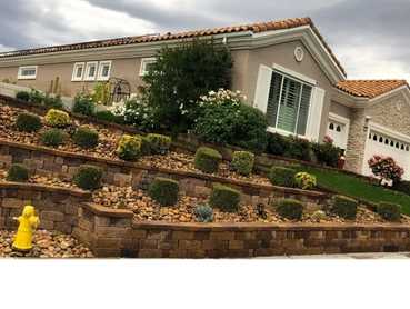 Terraced front yard with decorative shrubs and a yellow fire hydrant in front of a suburban house.