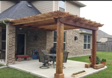Wooden pergola attached to a patio beside a brick house.