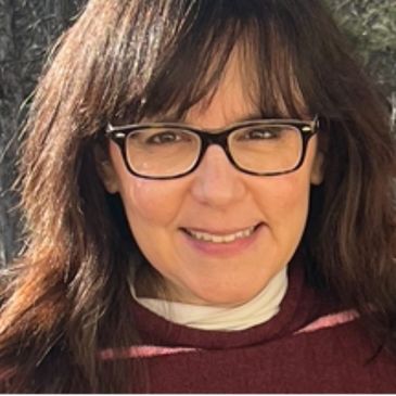 Smiling woman with glasses and brown hair in natural light.