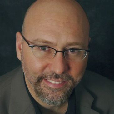 Smiling bald man with glasses and a beard in a suit jacket.