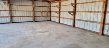 Empty barn interior with concrete floor and wooden beams.
