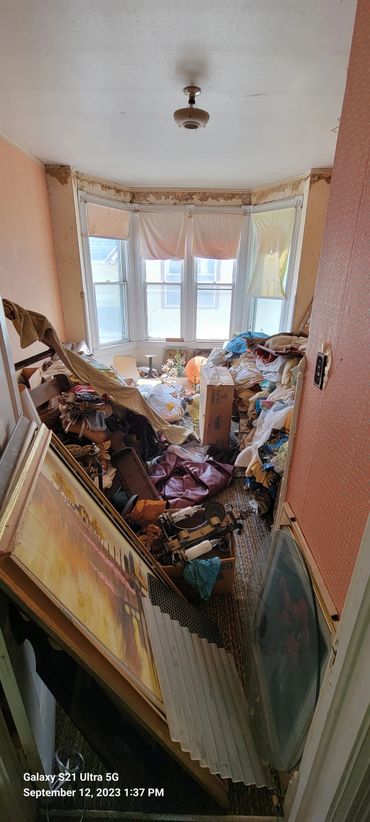 Cluttered room filled with various items and old furniture near a bay window.