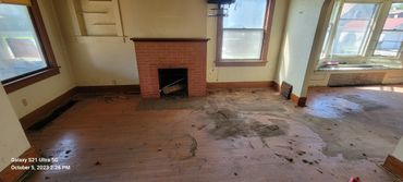 Empty, dirty room with a brick fireplace and large windows.