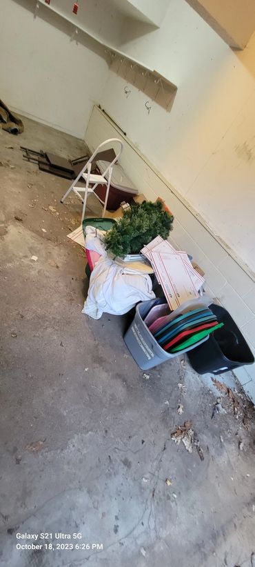 Cluttered storage area with assorted items and a white chair.