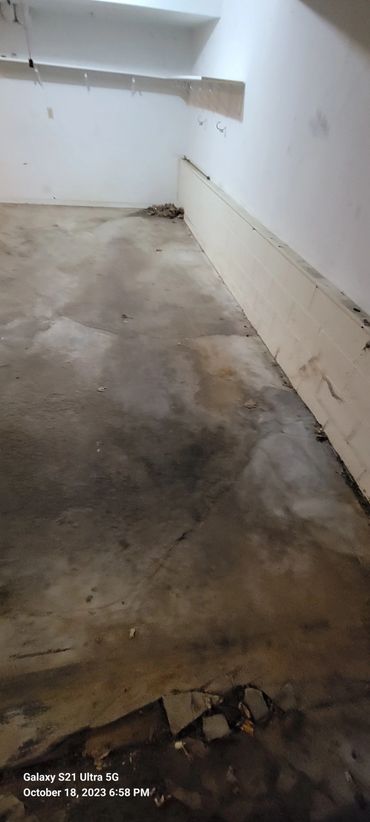 Empty room with stained and damaged concrete floor and white walls.