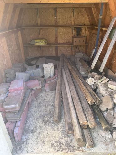 Storage shed with construction materials including bricks, wooden poles, and rocks.