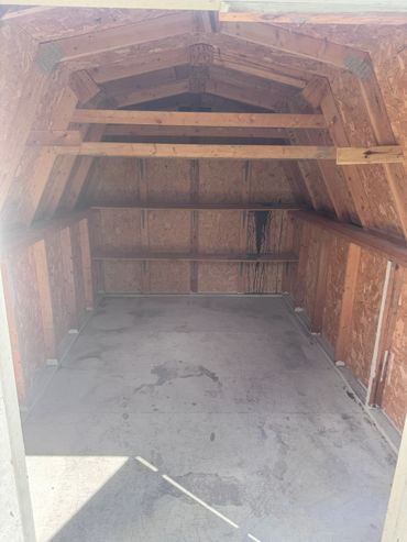 Empty wooden storage shed with concrete floor and triangular roof.
