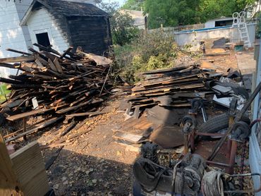 Burned shed and piles of charred debris in a backyard.