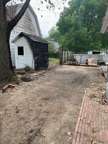 A small shed with fire damage next to a white house and an above-ground pool in a backyard.