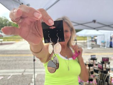 Woman holding up earrings at an outdoor market.