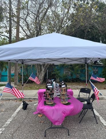 Outdoor market stall with jewelry and American flags under a white canopy.