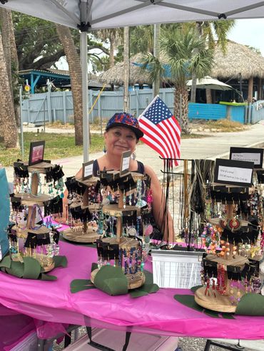 Woman selling colorful handmade jewelry under a tent with an American flag.