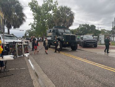 Sheriff vehicles and people gathered on a street with palm trees and cloudy sky.