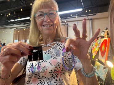 Smiling elderly woman showing handmade jewelry.