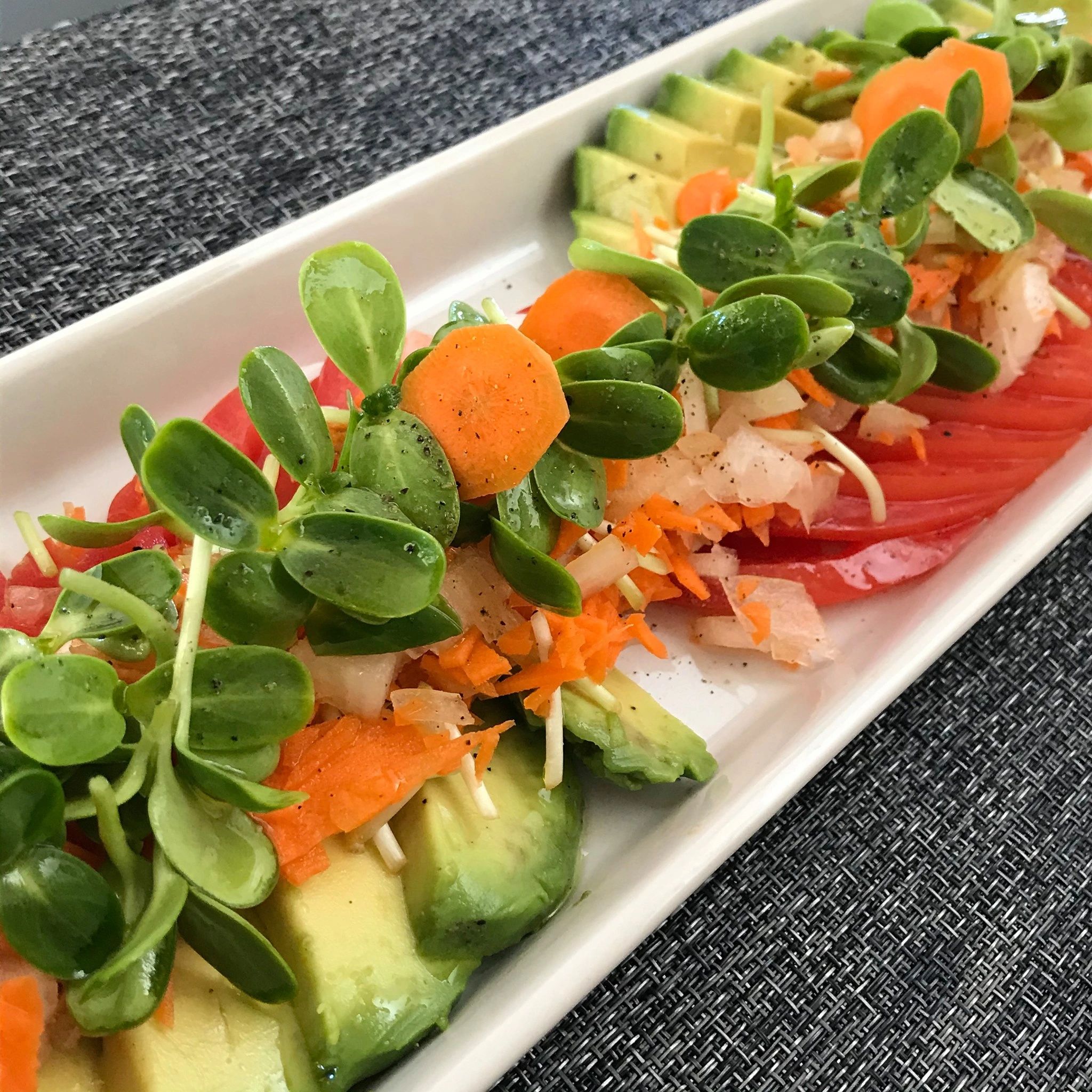 Appetizer with sliced avocado, tomato, carrot and onion. Topped with olive oil dressed Sunflowers.