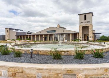 Modern winery building with a large circular fountain in front under a cloudy sky.
