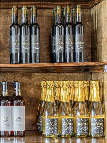 Shelves filled with various bottles of Arch Ray wine and champagne against a wooden backdrop.