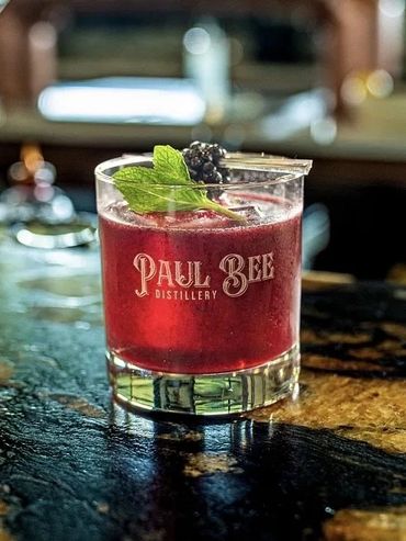 A vibrant red cocktail garnished with mint and berries in a Paul Bee Distillery glass.
