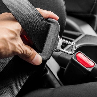 Hand holding a car seatbelt buckle near the seatbelt receiver.