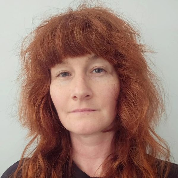 Woman with red curly hair and blue eyes looking at the camera.