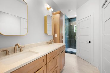 Double vanity master bedroom with custom gold medicine cabinets and vertical green tile shower