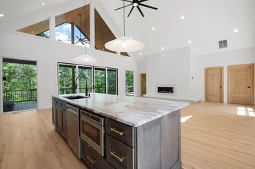 View from the kitchen of the open concept great room with giant slider, huge windows, and fire box