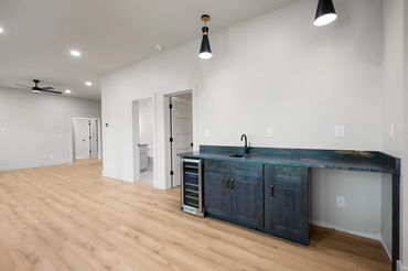 View of basement bar with granite countertop and terrace level living room, custom pendants & fan