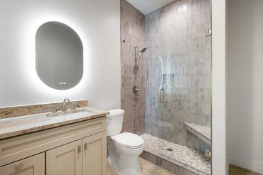 Custom vertical tile shower with glass shower doors, custom cabinetry with lighted mirror & granite