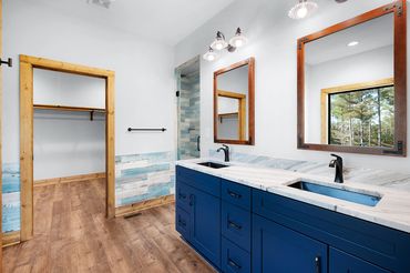 Two sinks in a blue vanity cabinet with 2 square mirrors & blue & brown tile & stained wood trim