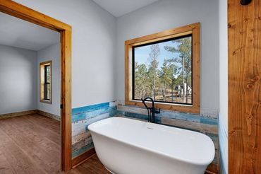 Stand alone tub under a large square window with blue & brown tile and stained wood trim