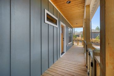 View down the covered wood porch walkway with stained tongue & groove ceiling and wood rails