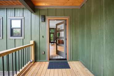 Modern style door with 4 glass panels and wood trim on the front porch of a forest green house