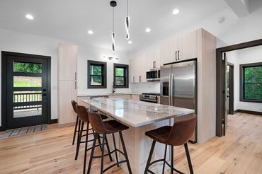 View of a modern open concept front door and kitchen with a granite topped island & modern pendants