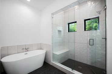 Stand alone white tub and walk in shower with vertical white tile and black herringbone floor tile