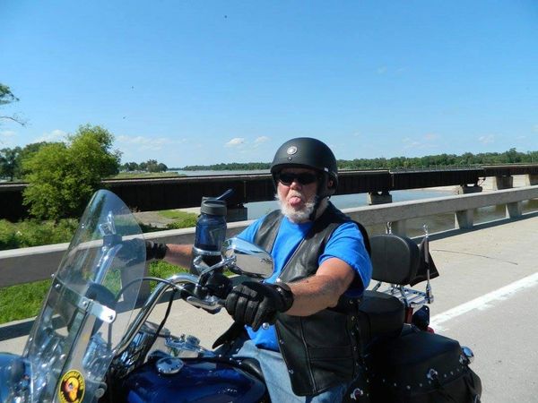 Older man on motorcycle sticking out his tongue on a sunny day.
