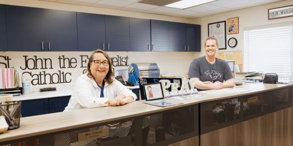 Two women smiling behind a front desk at St John the Evangelist Catholic.