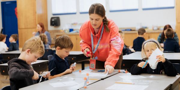 Teacher assists children with cutting paper.