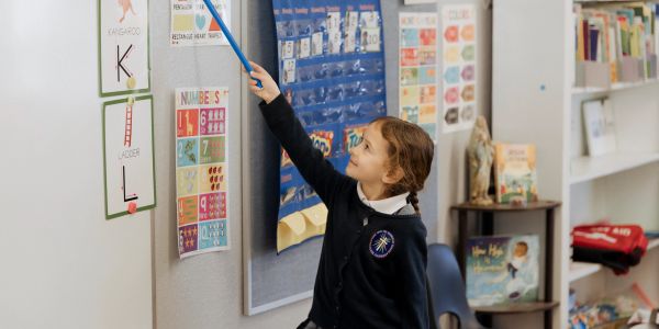Young girl pointing at educational posters in classroom.
