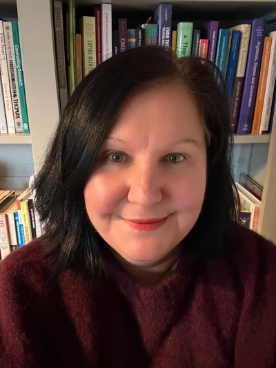 Woman with dark hair smiling in front of bookshelves.