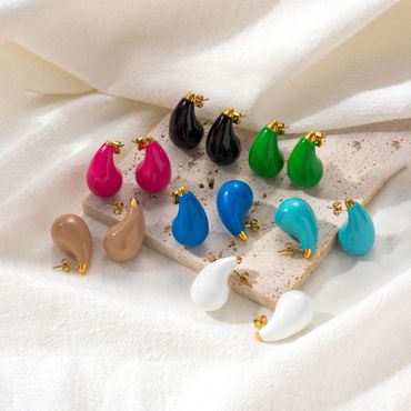 Colorful teardrop-shaped earrings with gold accents arranged on a stone slab.
