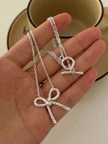 Hand holding a silver bow-shaped necklace with a toggle clasp.